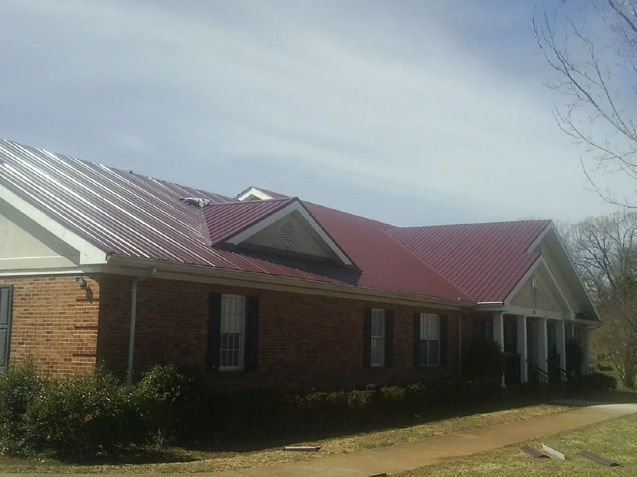 Red metal roof with gabled entries on a long brick building, from a Hail Damage Roof Repair job in Tallassee