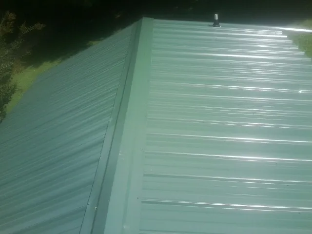 New green metal panels meeting at the ridge of a roof — Flat Roof Repair work by our crew in Tallassee