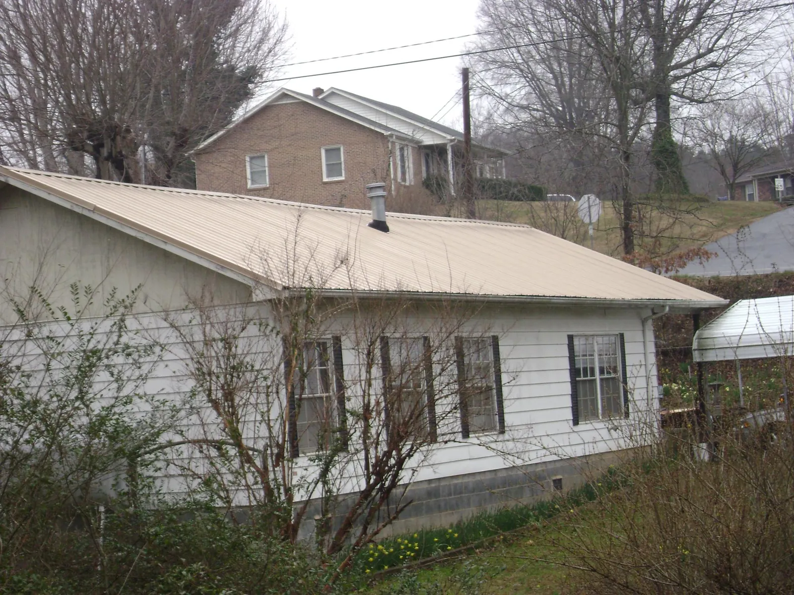 Tan metal roof on a white sided house set into a hillside — Commercial Roofing by Roofing Brothers in Tallassee