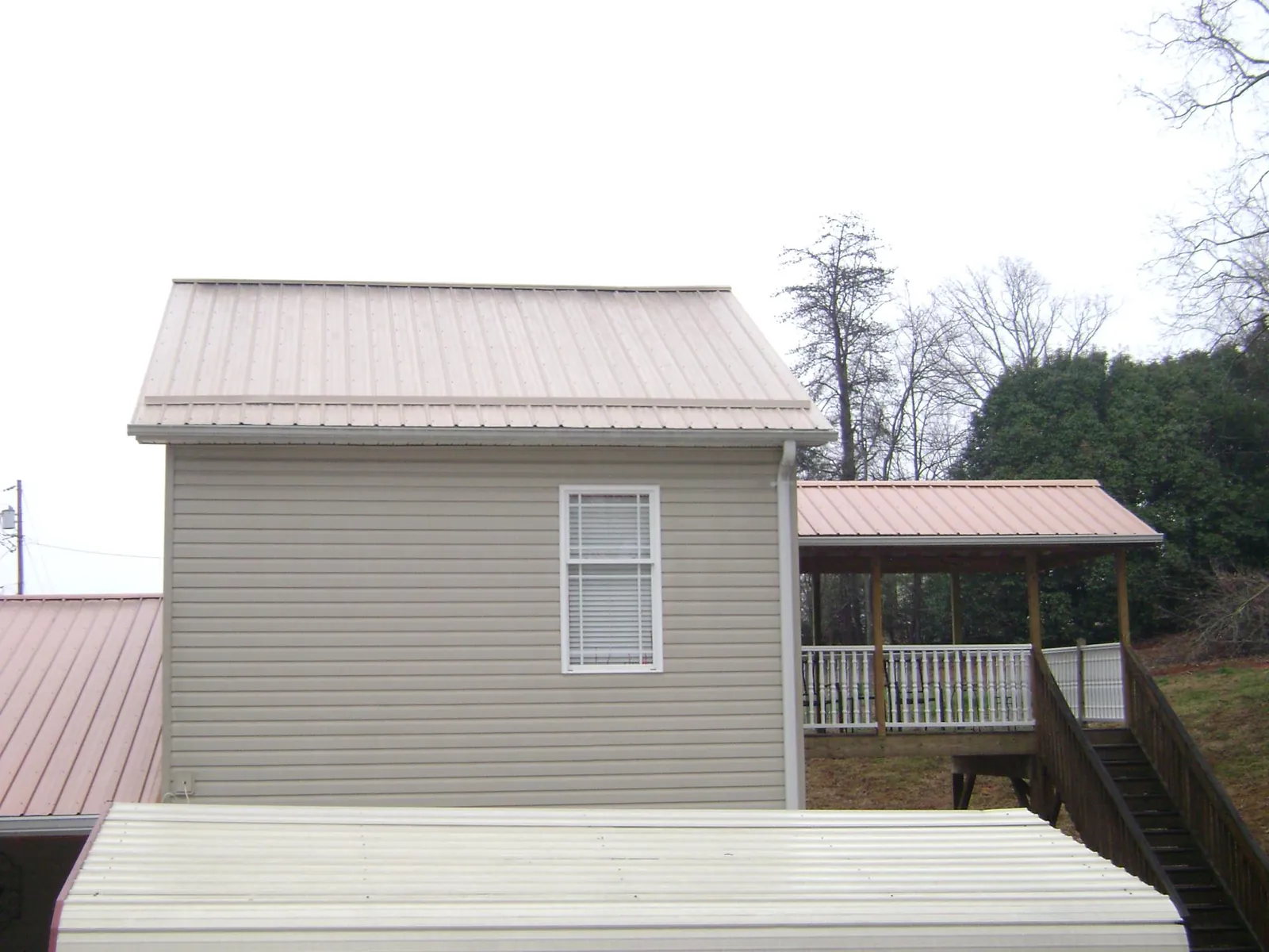 Tan metal roofs on a two story addition and attached porch, from a Roof Replacement job in Tallassee